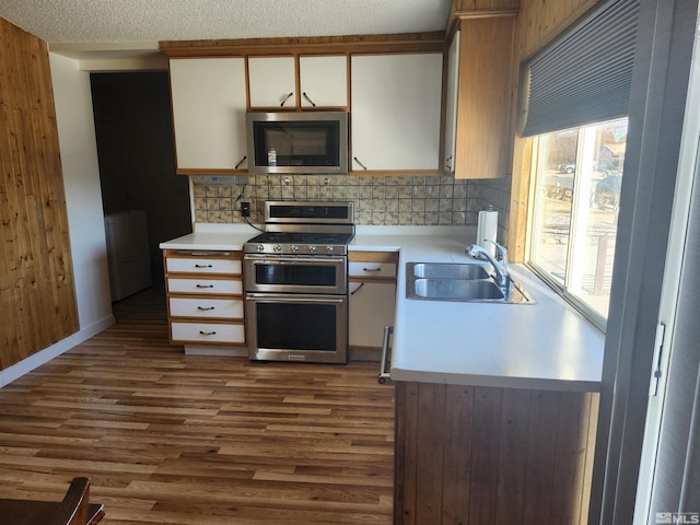 kitchen with hardwood / wood-style floors, washer / clothes dryer, white cabinetry, stainless steel appliances, and sink