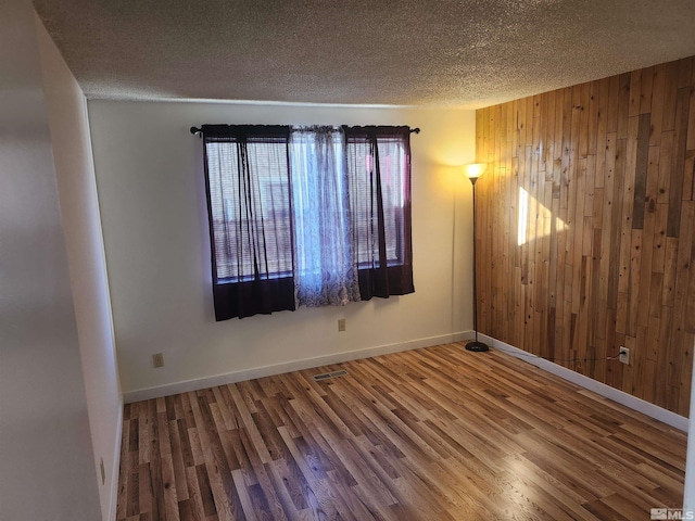 unfurnished room with a textured ceiling, wood-type flooring, and wooden walls