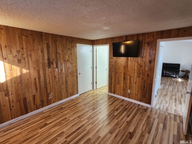 unfurnished room with a textured ceiling, light wood-type flooring, and wooden walls