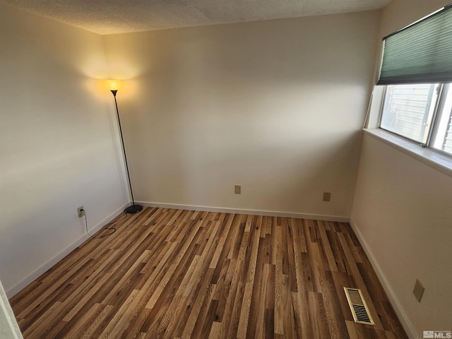 unfurnished room featuring dark wood-type flooring and a textured ceiling