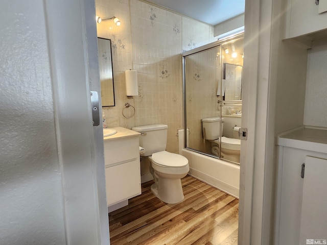 full bathroom with toilet, vanity, tile walls, hardwood / wood-style floors, and enclosed tub / shower combo