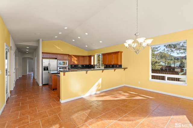 kitchen featuring backsplash, kitchen peninsula, hanging light fixtures, appliances with stainless steel finishes, and a breakfast bar area