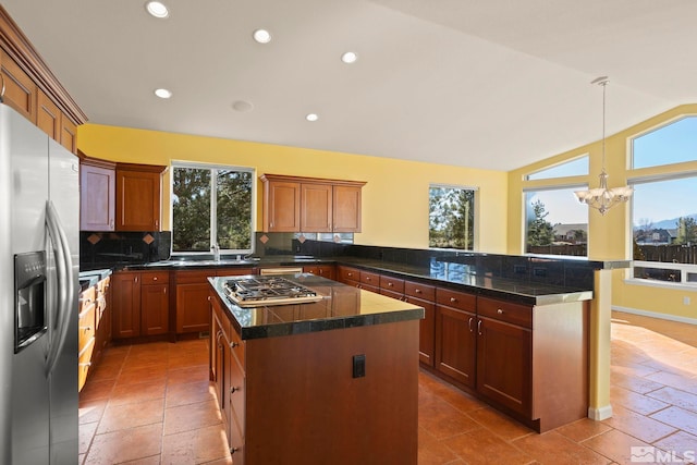 kitchen featuring kitchen peninsula, appliances with stainless steel finishes, backsplash, vaulted ceiling, and a center island