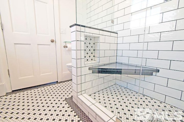 bathroom with toilet, tile patterned flooring, and a tile shower