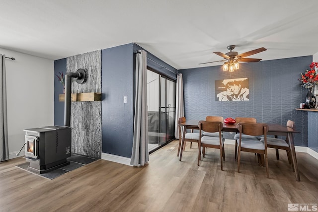 dining space with hardwood / wood-style flooring, a wood stove, and ceiling fan