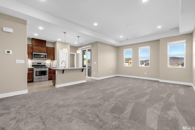 kitchen with hanging light fixtures, light colored carpet, appliances with stainless steel finishes, and a center island with sink