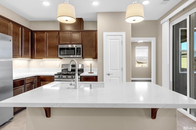 kitchen with a kitchen bar, hanging light fixtures, appliances with stainless steel finishes, and a center island with sink