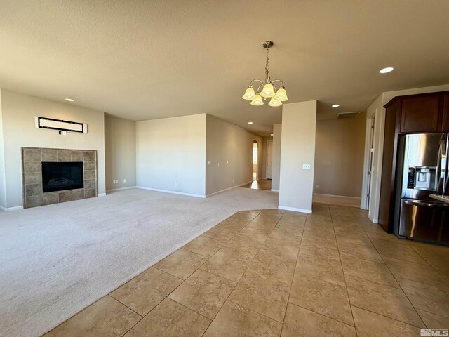 unfurnished living room featuring a fireplace, light colored carpet, and a notable chandelier