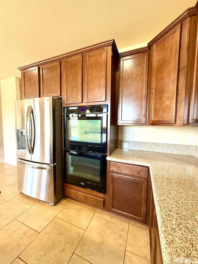 kitchen with light tile patterned flooring, light stone countertops, stainless steel fridge, and double oven