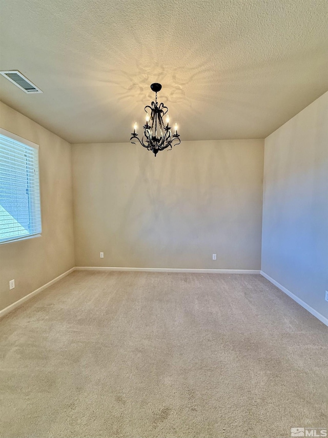 spare room with light carpet, a textured ceiling, and a notable chandelier