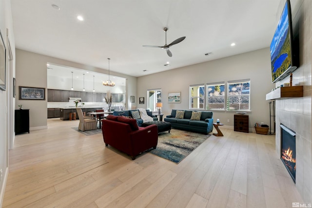 living room with ceiling fan with notable chandelier, a tile fireplace, and light hardwood / wood-style flooring