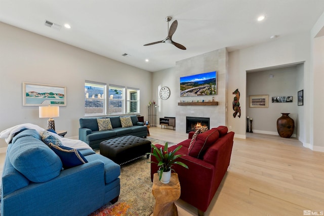 living room featuring a fireplace, light hardwood / wood-style floors, and ceiling fan