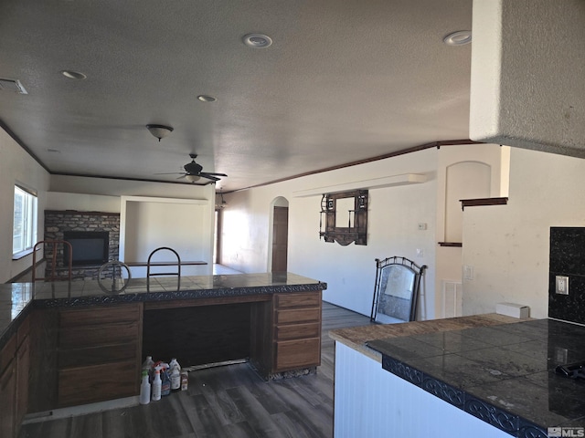 kitchen with ceiling fan, a textured ceiling, dark hardwood / wood-style floors, and a fireplace