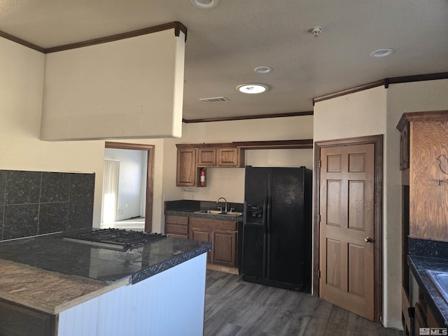 kitchen with kitchen peninsula, sink, dark hardwood / wood-style floors, black refrigerator with ice dispenser, and stainless steel gas cooktop