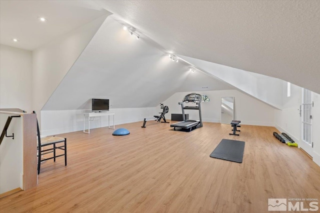 workout room with light hardwood / wood-style floors, a textured ceiling, and vaulted ceiling