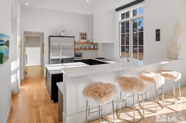 kitchen featuring kitchen peninsula, tasteful backsplash, light stone countertops, built in refrigerator, and a kitchen bar