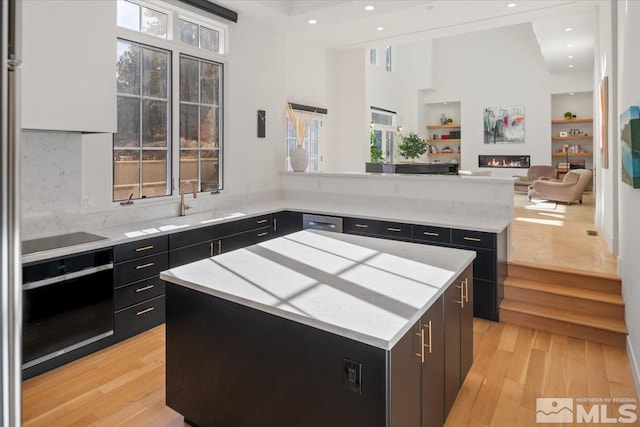 kitchen featuring sink, oven, a center island, black electric cooktop, and light hardwood / wood-style floors