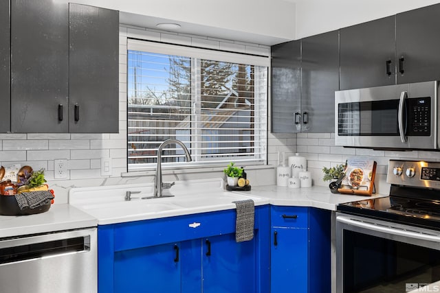 kitchen featuring light stone countertops, appliances with stainless steel finishes, sink, backsplash, and blue cabinets