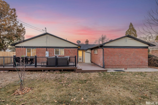 back house at dusk featuring a deck and a lawn