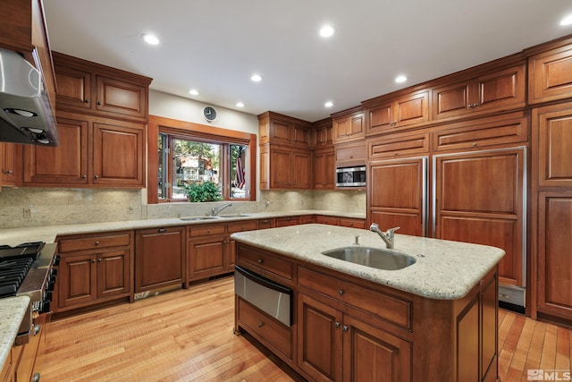 kitchen featuring light stone countertops, sink, stainless steel microwave, and a center island with sink