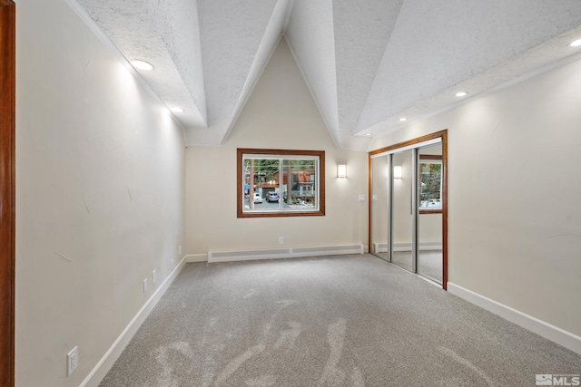 carpeted empty room featuring a textured ceiling, a baseboard heating unit, and vaulted ceiling