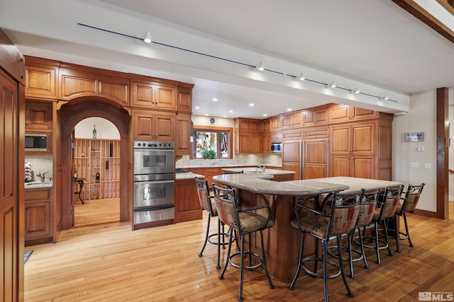 kitchen with a spacious island, a kitchen bar, built in appliances, decorative backsplash, and light hardwood / wood-style flooring