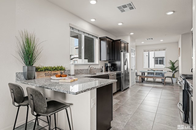 kitchen with kitchen peninsula, appliances with stainless steel finishes, light tile patterned floors, light stone countertops, and a breakfast bar area