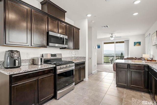 kitchen with appliances with stainless steel finishes, light carpet, dark brown cabinetry, ceiling fan, and light stone counters