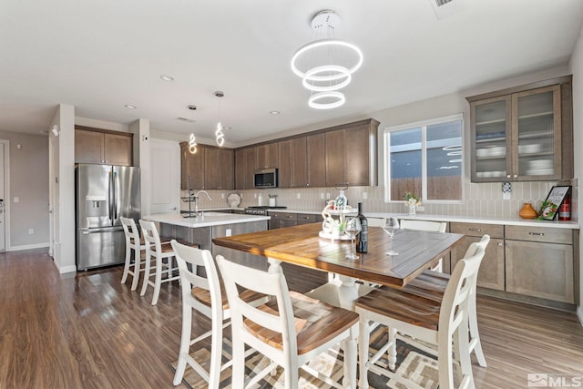 kitchen with appliances with stainless steel finishes, hanging light fixtures, backsplash, a center island with sink, and dark hardwood / wood-style floors