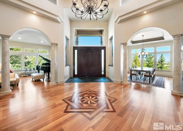 entrance foyer with a towering ceiling, a chandelier, ornate columns, and hardwood / wood-style floors