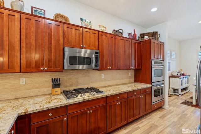 kitchen featuring light stone counters, appliances with stainless steel finishes, tasteful backsplash, and light wood-type flooring