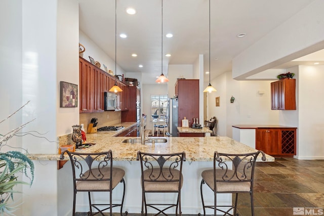 kitchen with kitchen peninsula, hanging light fixtures, sink, light stone countertops, and stainless steel appliances