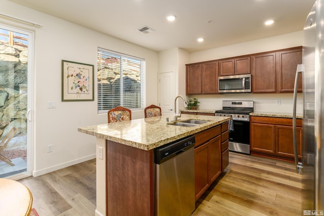 kitchen featuring sink, light stone countertops, a center island with sink, light hardwood / wood-style floors, and stainless steel appliances