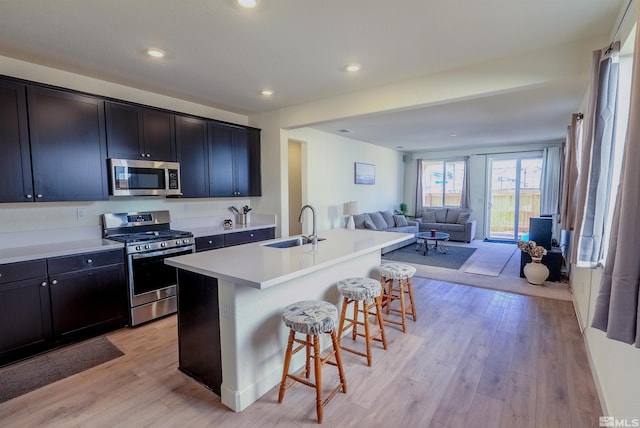 kitchen featuring appliances with stainless steel finishes, light wood-type flooring, sink, a center island with sink, and a breakfast bar area