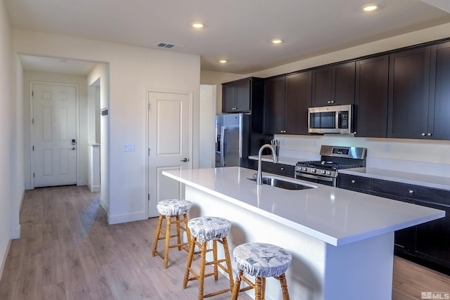 kitchen with appliances with stainless steel finishes, a kitchen breakfast bar, sink, light wood-type flooring, and an island with sink