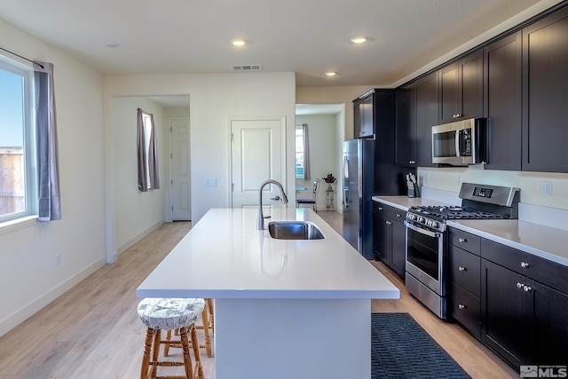 kitchen featuring light hardwood / wood-style floors, sink, a breakfast bar, stainless steel appliances, and a center island with sink