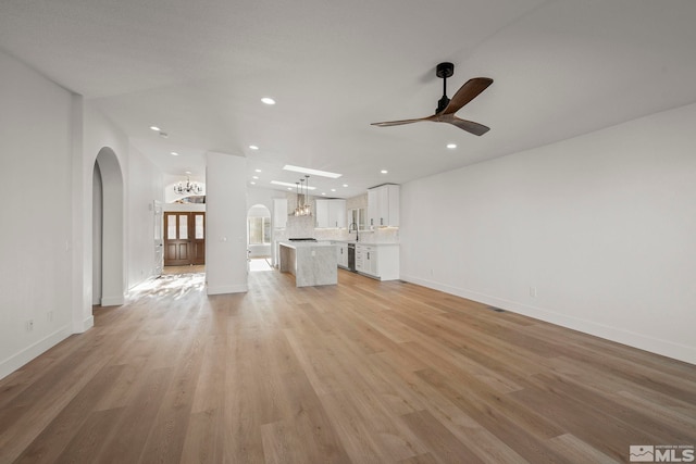 unfurnished living room featuring ceiling fan with notable chandelier and light wood-type flooring