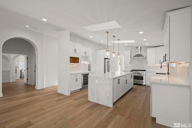 kitchen featuring wall chimney exhaust hood, high quality appliances, white cabinets, a kitchen island, and beverage cooler