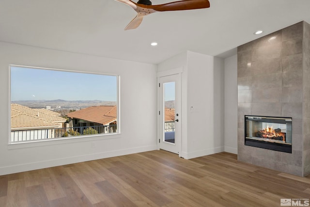 unfurnished living room with hardwood / wood-style floors, ceiling fan, vaulted ceiling, a mountain view, and a tiled fireplace