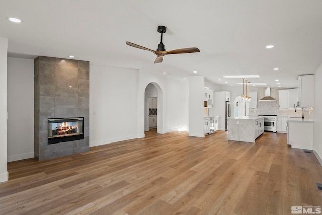 unfurnished living room with light hardwood / wood-style floors, sink, a tile fireplace, and ceiling fan