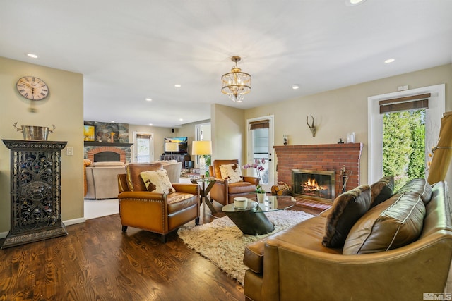 living room featuring a notable chandelier, dark hardwood / wood-style floors, and a brick fireplace