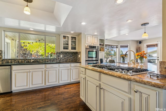 kitchen with pendant lighting, dark hardwood / wood-style flooring, appliances with stainless steel finishes, a wealth of natural light, and dark stone countertops