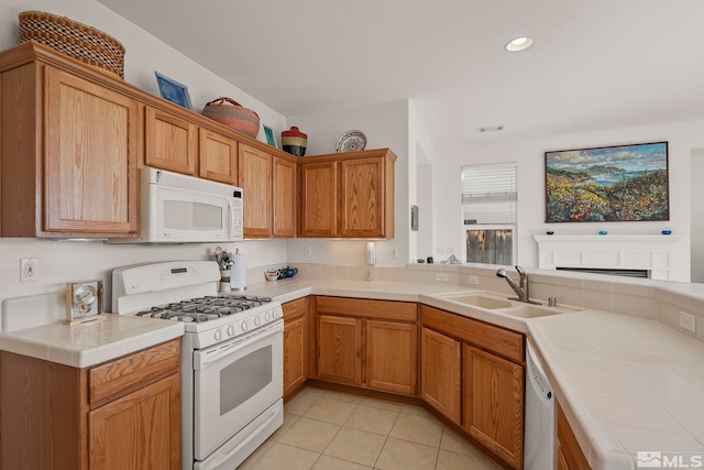 kitchen featuring kitchen peninsula, sink, light tile patterned flooring, white appliances, and tile counters