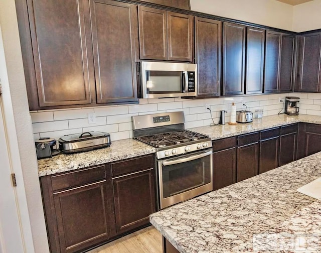 kitchen featuring stainless steel appliances, light stone counters, and backsplash