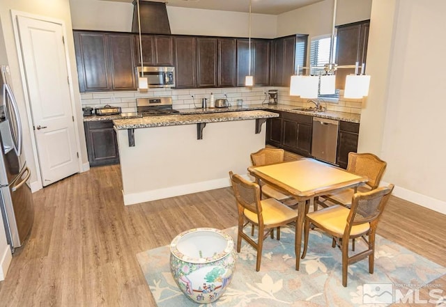 kitchen featuring a center island, dark brown cabinets, decorative light fixtures, stainless steel appliances, and light stone counters