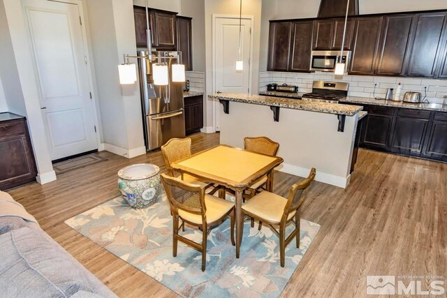 kitchen featuring decorative light fixtures, light stone counters, appliances with stainless steel finishes, and a breakfast bar area