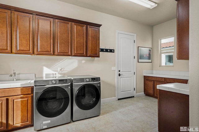 clothes washing area featuring sink, washing machine and dryer, light tile patterned floors, and cabinets