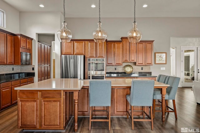 kitchen with a kitchen island, stainless steel appliances, backsplash, hanging light fixtures, and a breakfast bar