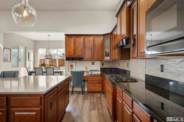 kitchen featuring ventilation hood, backsplash, hanging light fixtures, and wood-type flooring