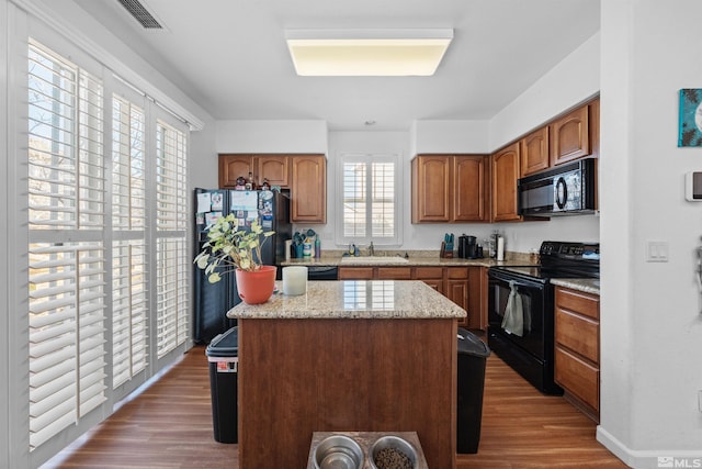 kitchen with black appliances, hardwood / wood-style flooring, a center island, and sink